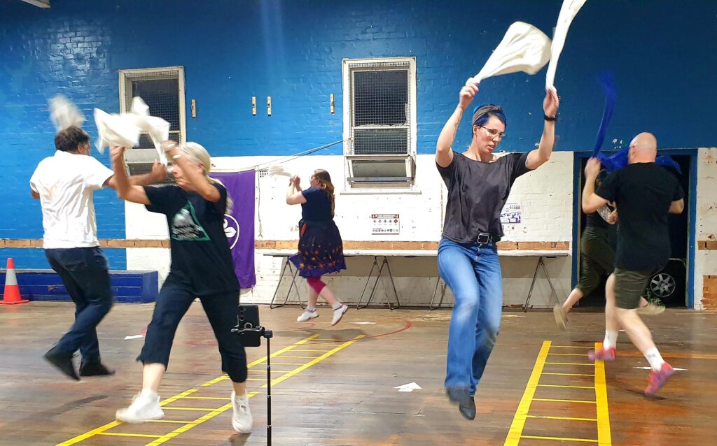 Dancers in casual clothes jump while waving hankies